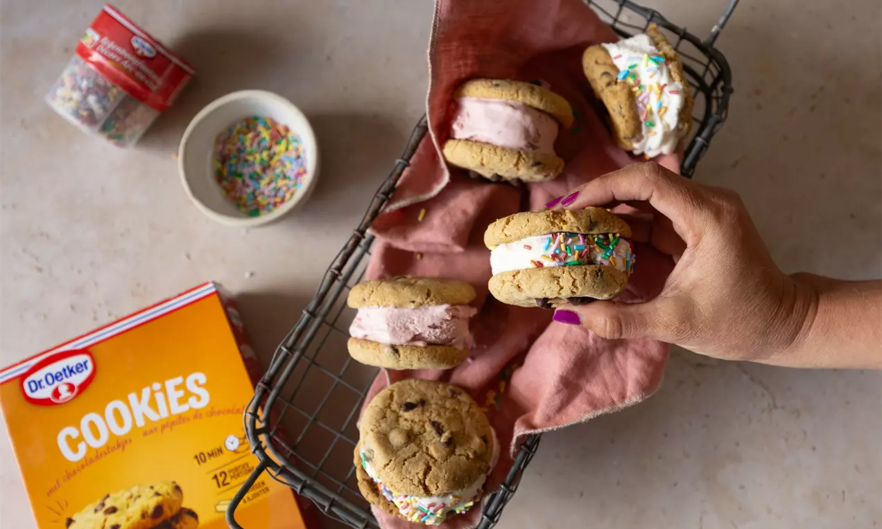 Glaces aux cookies garnies de crème rose et blanche avec vermicelles colorés, dans un panier métallique tapissé de tissu rose