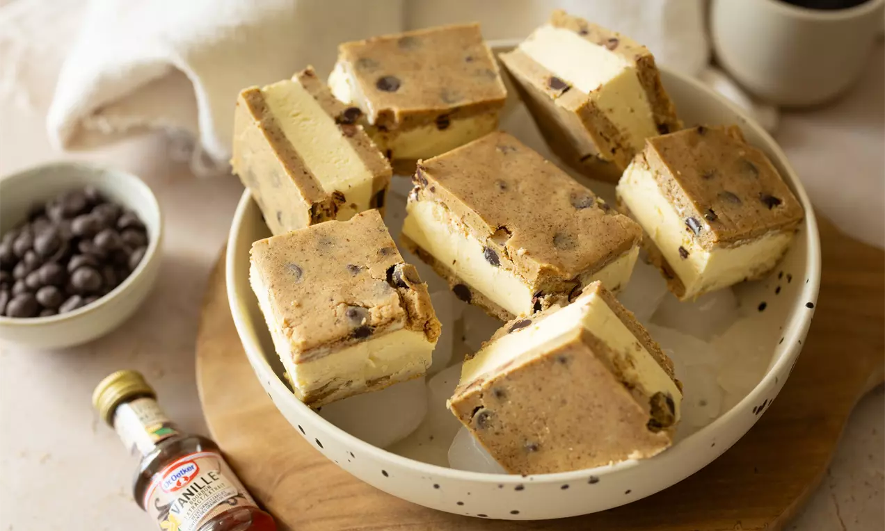 Carrés de crème vanillée entre deux couches de biscuit moelleux aux pépites de chocolat, présentés sur une assiette blanche à motifs