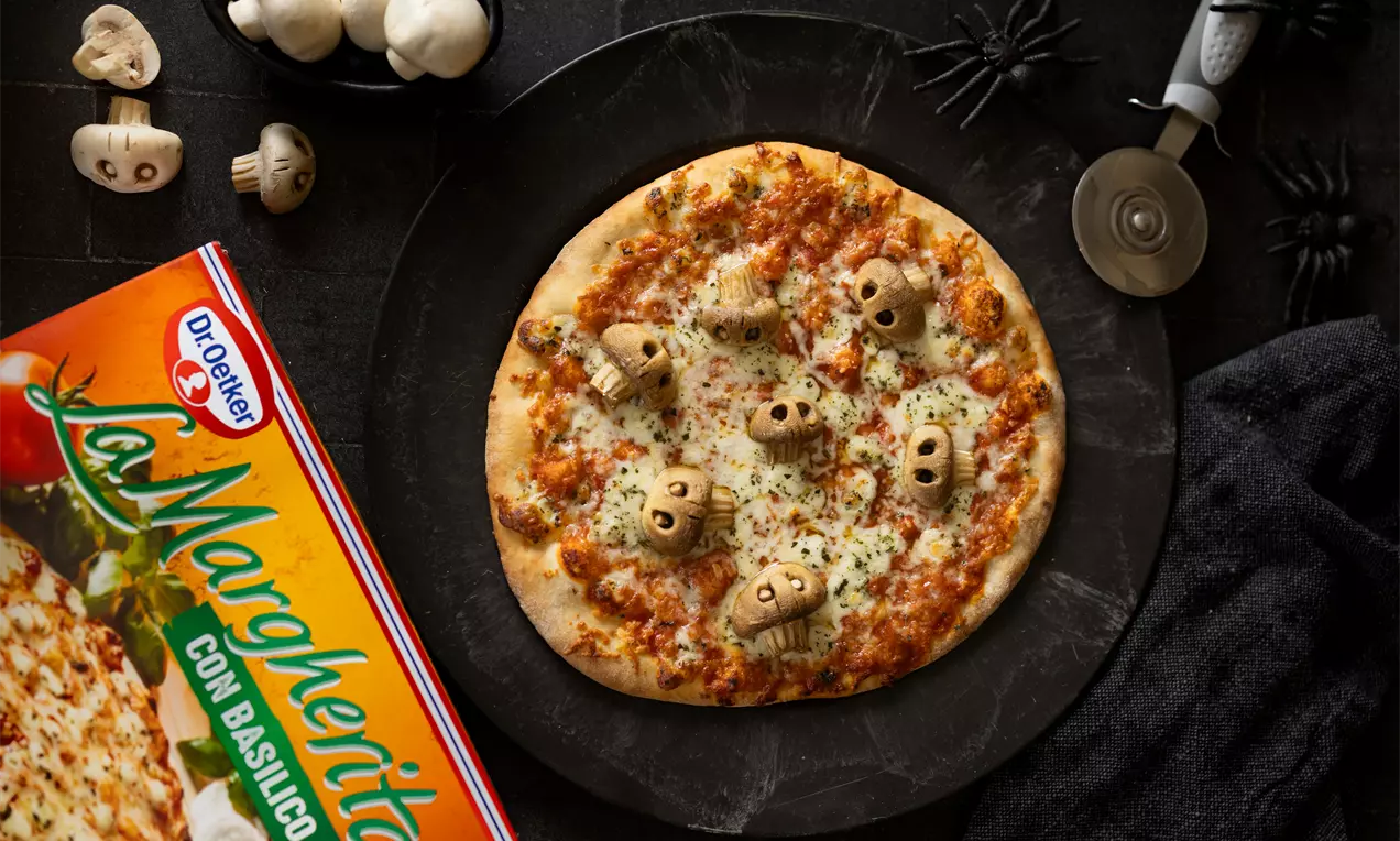 Halloween-pizza met goudbruine korst, gesmolten kaas en champignons in schedelvorm, geserveerd op een zwarte schaal met decoraties
