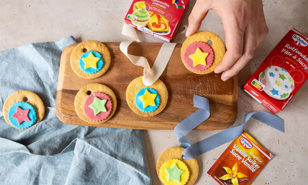 Biscuits ronds aux couleurs vives décorés d'étoiles en pâte à sucre jaune, bleue et rose sur une planche en bois avec rubans