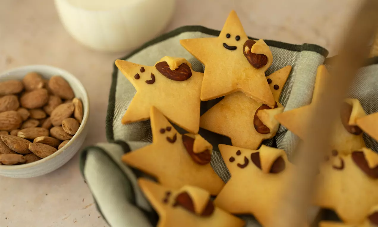 Petits biscuits colorés doré en forme d'étoiles souriantes, décorés de chocolat et d'amandes, posés sur un linge avec des amandes à côté