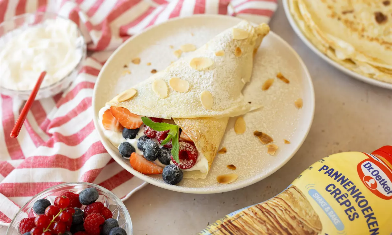 Crêpes dorées enroulées en cornet garnies de fruits rouges et myrtilles, décorées d'amandes effilées sur une assiette blanche