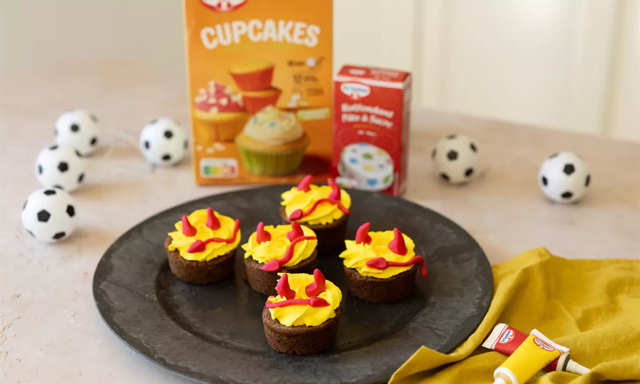 Cupcakes chocolat couverts de crème jaune vif avec flammes rouges sur plateau gris, entourés de mini ballons de football