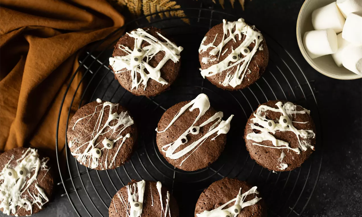 Biscuits moelleux chocolatés ronds, décorés de filets de chocolat blanc et d’yeux en sucre, disposés sur une grille noire