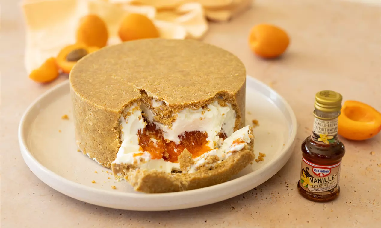 Ronde cheesecake met beige koekbodem, een hap eruit onthult witte roomkaasvulling en oranje abrikozencompote op een wit bord