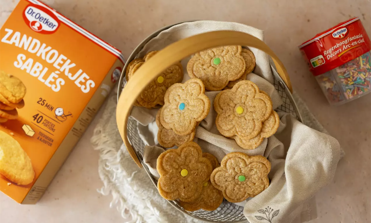 Biscuits dorés en forme de fleur avec des pastilles colorées au centre disposés dans un panier en métal doublé de tissu écru